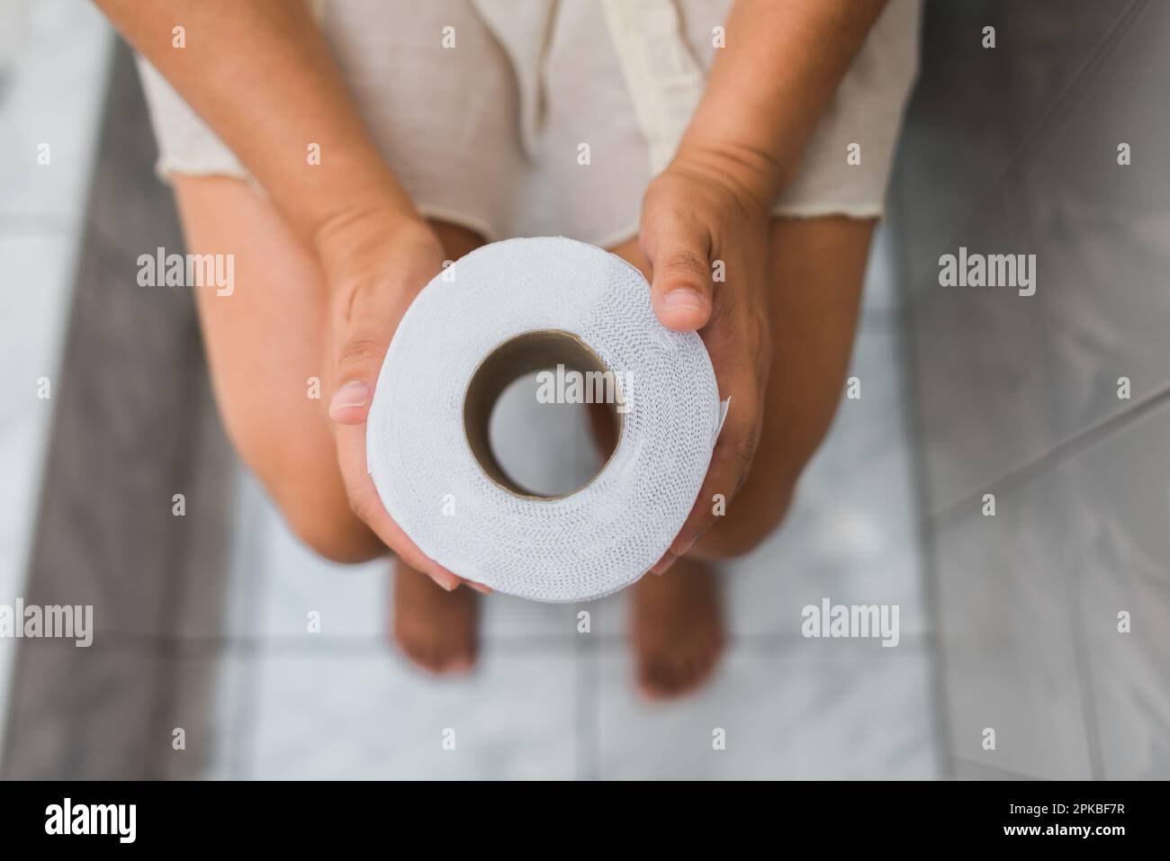 shot from above of a toilet paper in the hands of an unknown woman sitting barefoot on her toilet paper Stock Photo