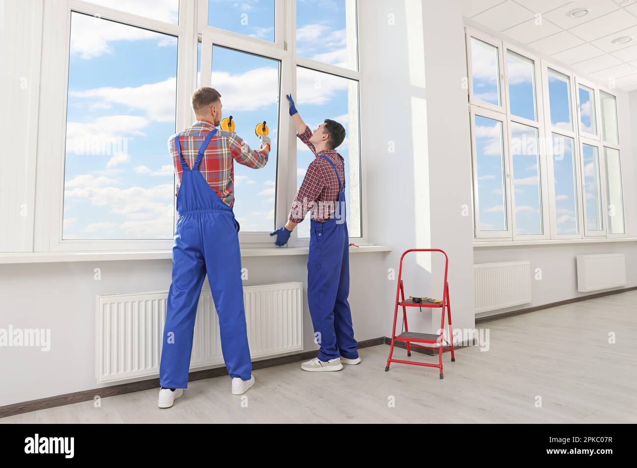Workers using suction lifters during plastic window installation indoors Stock Photo