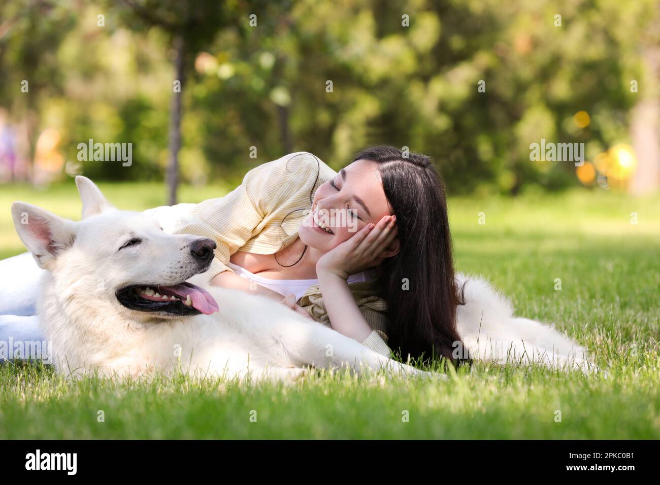 Teenage girl lying with her white Swiss Shepherd dog on green grass in ...