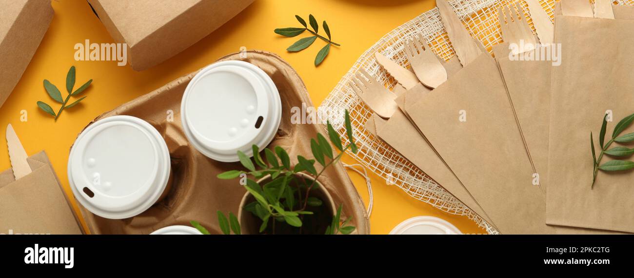 Paper and wooden tableware with green twigs on yellow background, flat ...