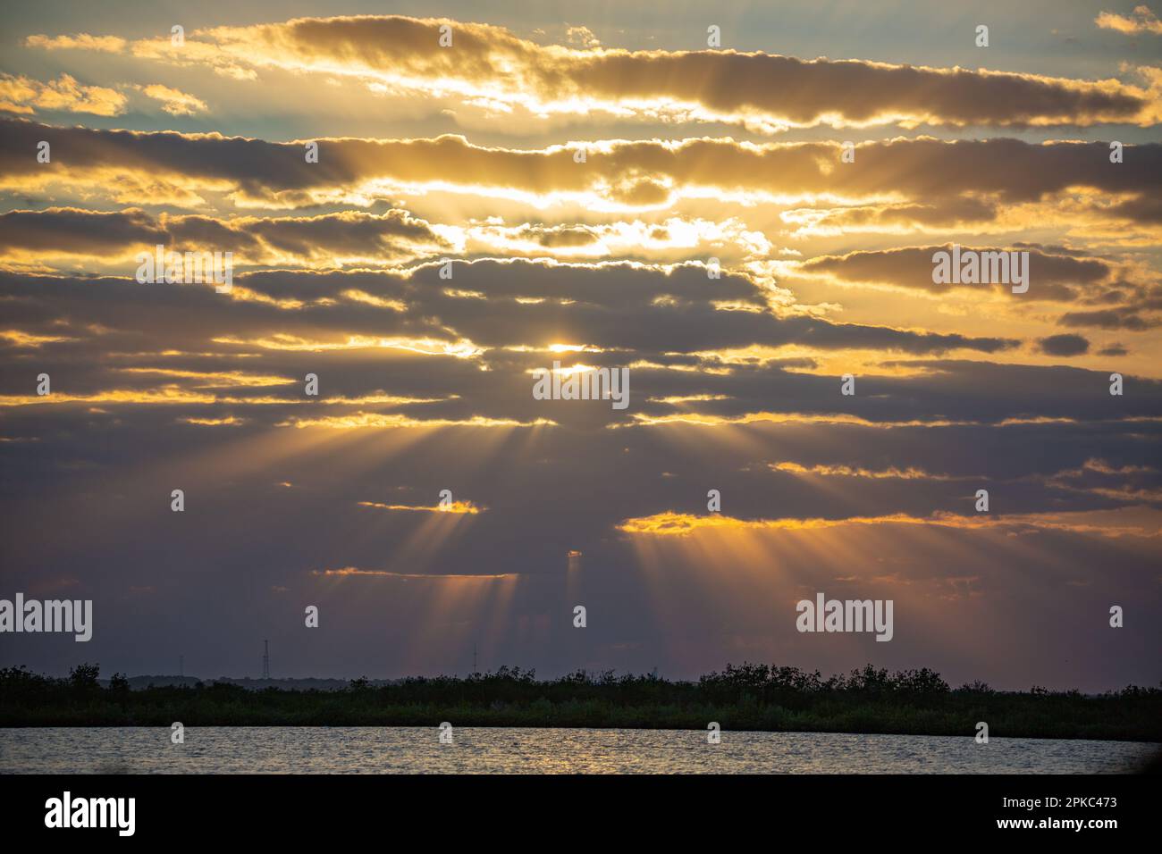 a picture of a cloudy sky and a sunset, the sun rays are glowing through the clouds. Lake and the horizon on the bottom part. Stock Photo