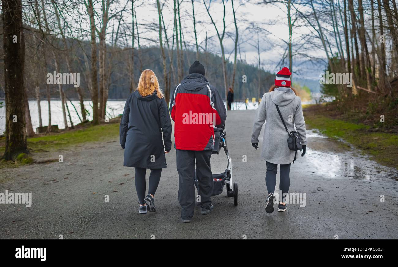 Happy family taking a walk in a park, back view. Family walking together along forest path with their child, father pushing the pram. young people wal Stock Photo