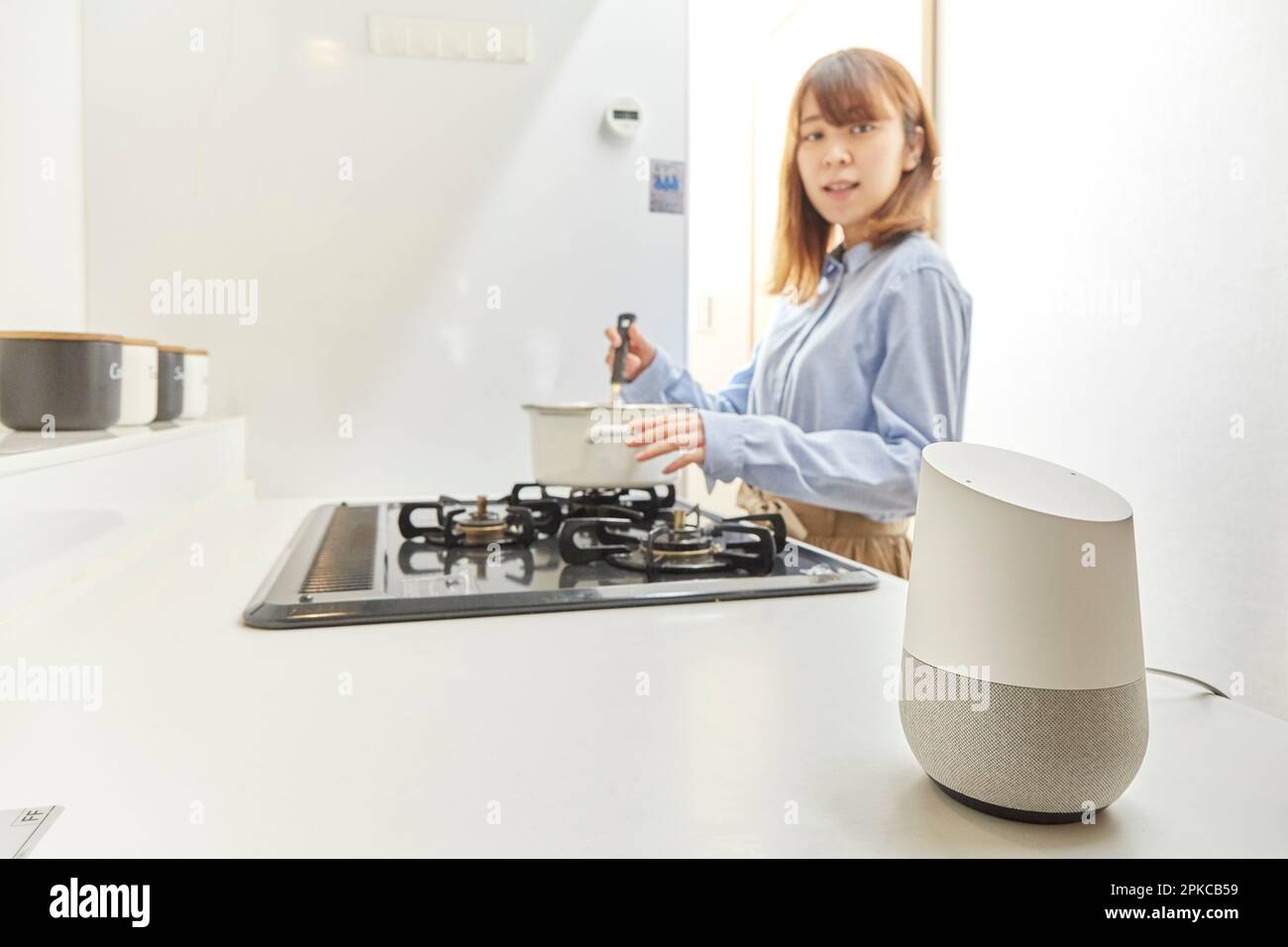 Woman talking to AI speaker while cooking in the kitchen Stock Photo