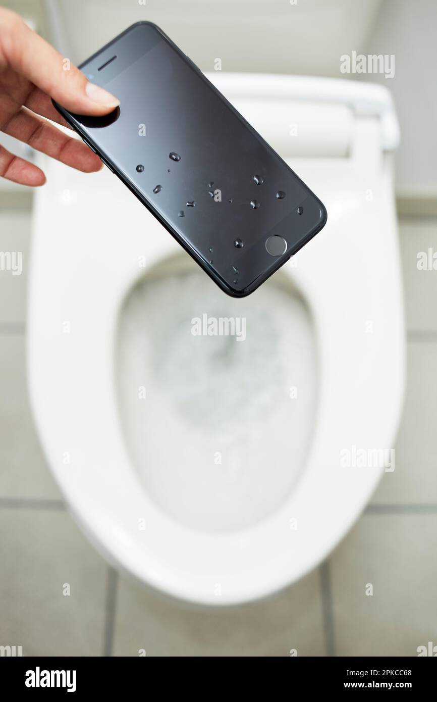 Hands picking up a cell phone that has fallen into the toilet bowl