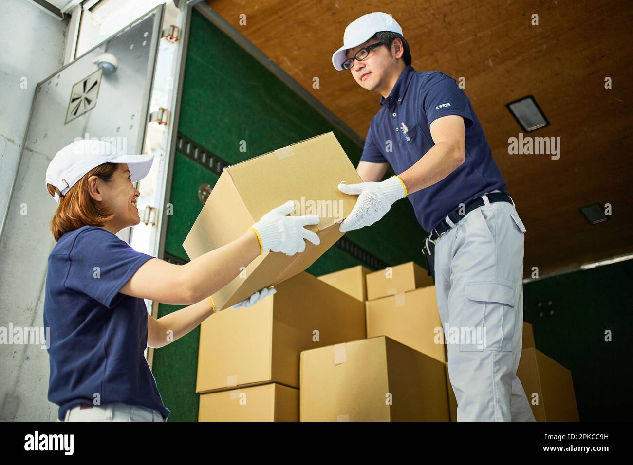 Man and woman in work clothes unloading cardboard boxes from a truck Stock Photo
