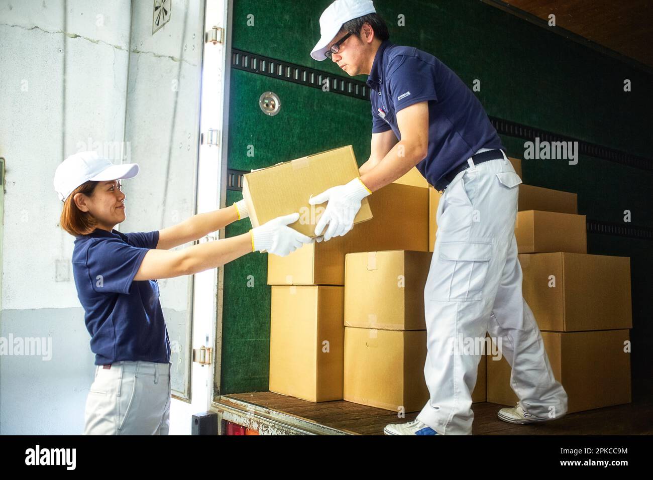 Man and woman in work clothes unloading cardboard boxes from a truck Stock Photo