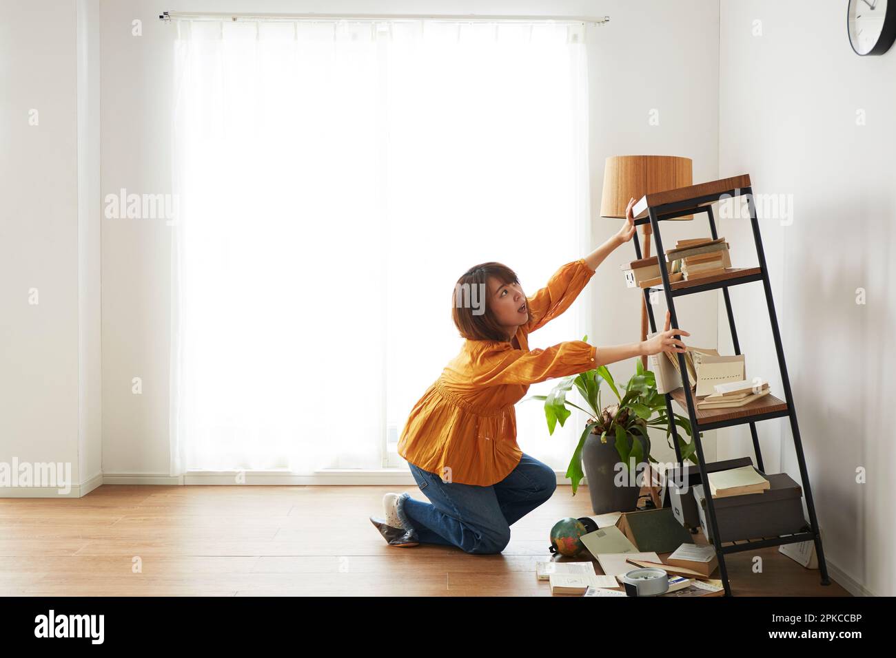 Woman supporting a bookshelf that collapsed during an earthquake Stock