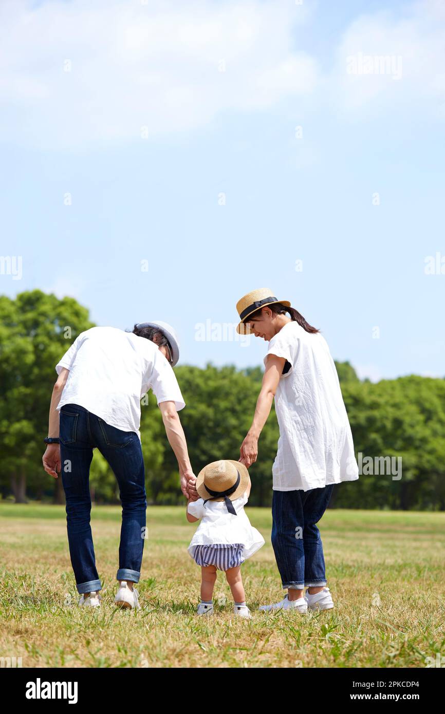 Baby and parents walking side by side on grass Stock Photo