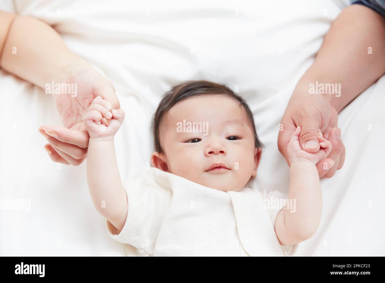 Mother and father holding hands with baby sleeping on white sheets