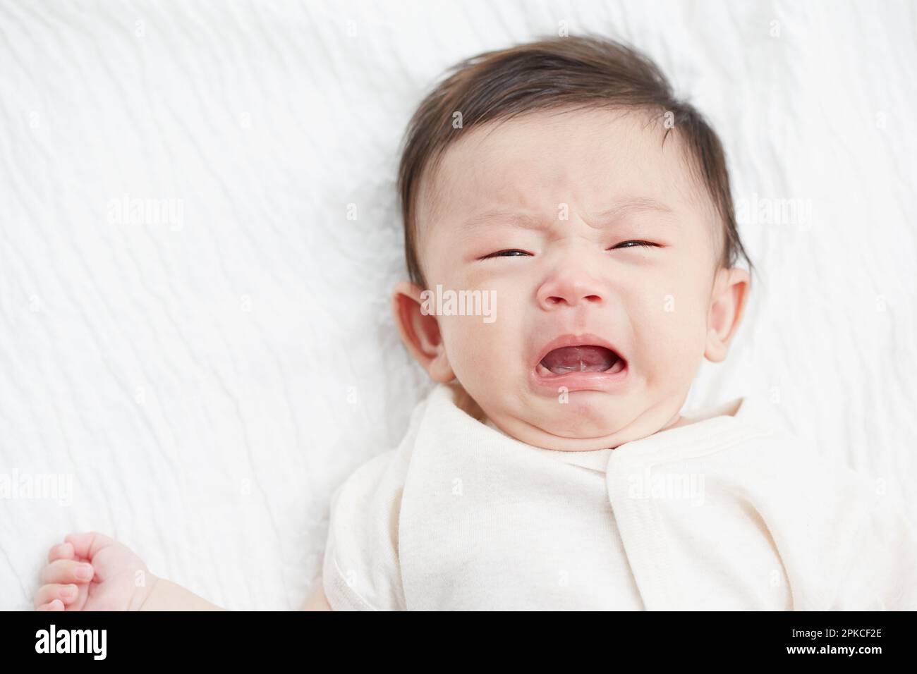 Baby about to cry on white sheets Stock Photo