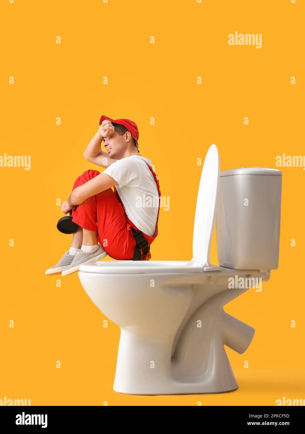 Young plumber with plunger and toilet bowl on yellow background Stock