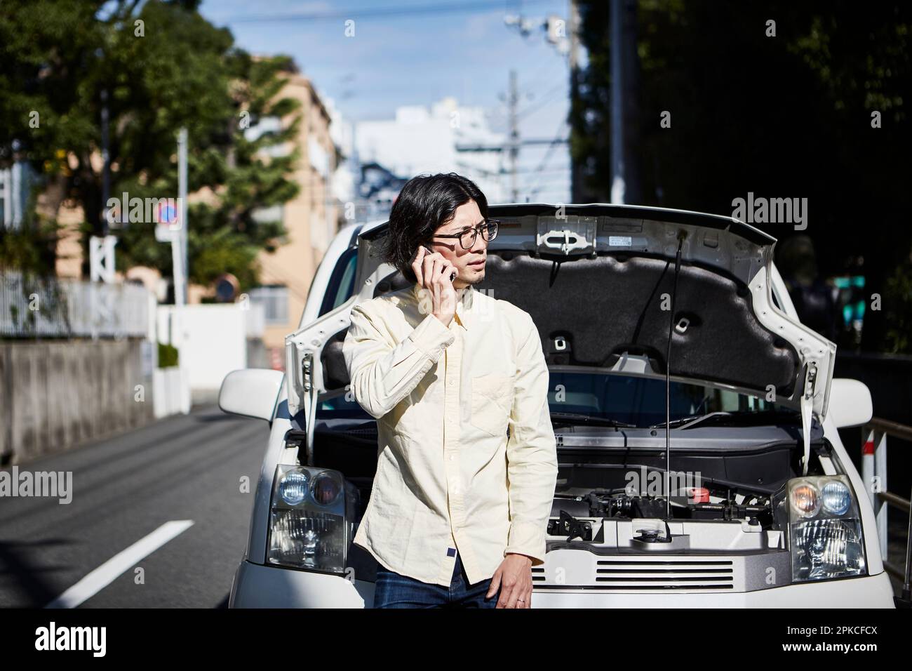 Man making a phone call in front of a car with its hood open Stock Photo