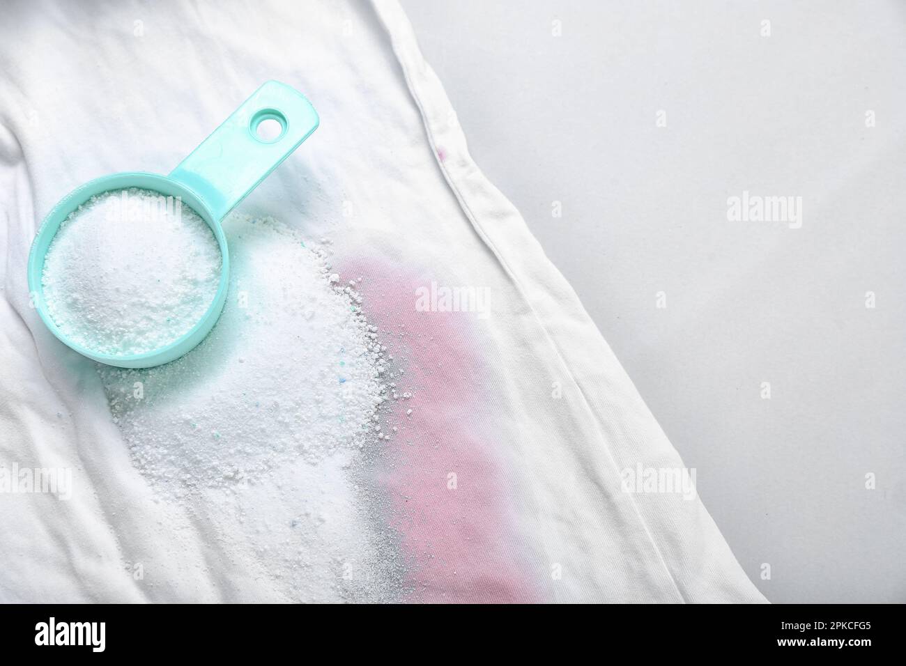 Laundry detergent with stained clothes on light background, closeup