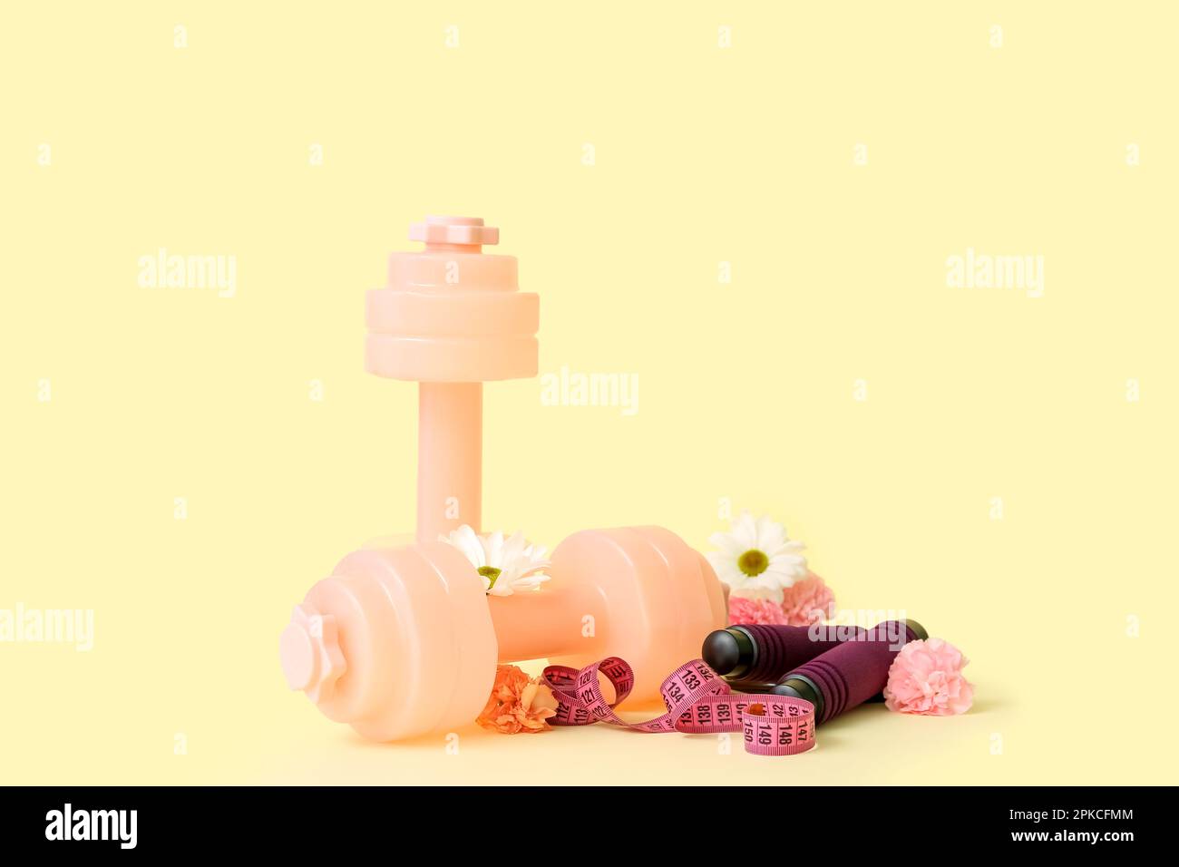 Dumbbells with skipping rope, tape measure and spring flowers on yellow