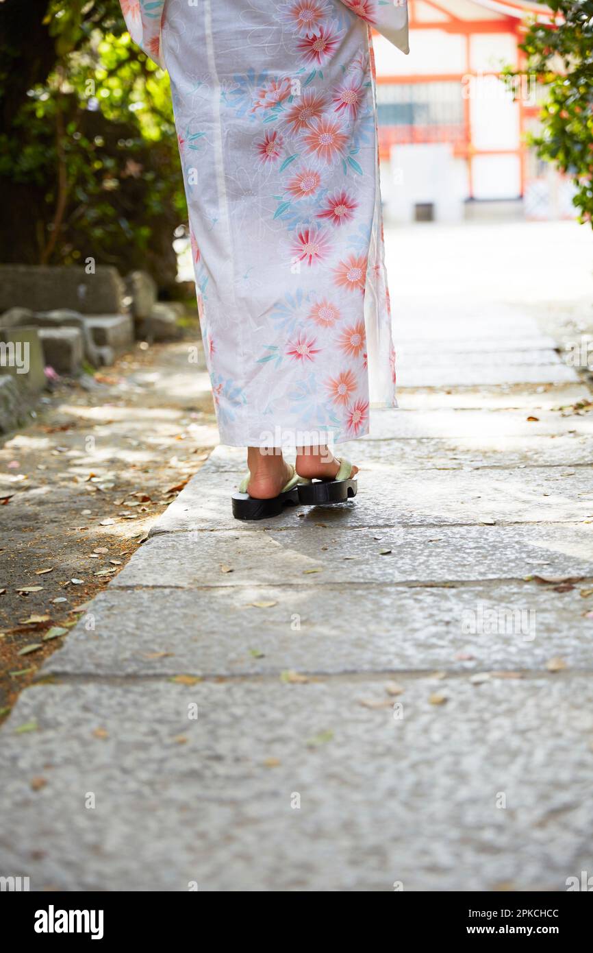 Woman's back feet walking on cobblestone pavement in yukata Stock Photo