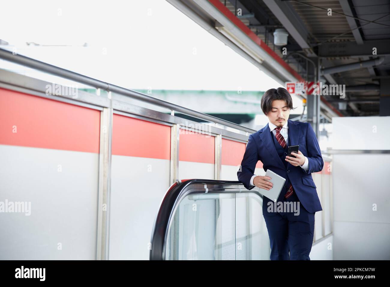 Man in suit looking at smartphone on escalator at train station Stock Photo