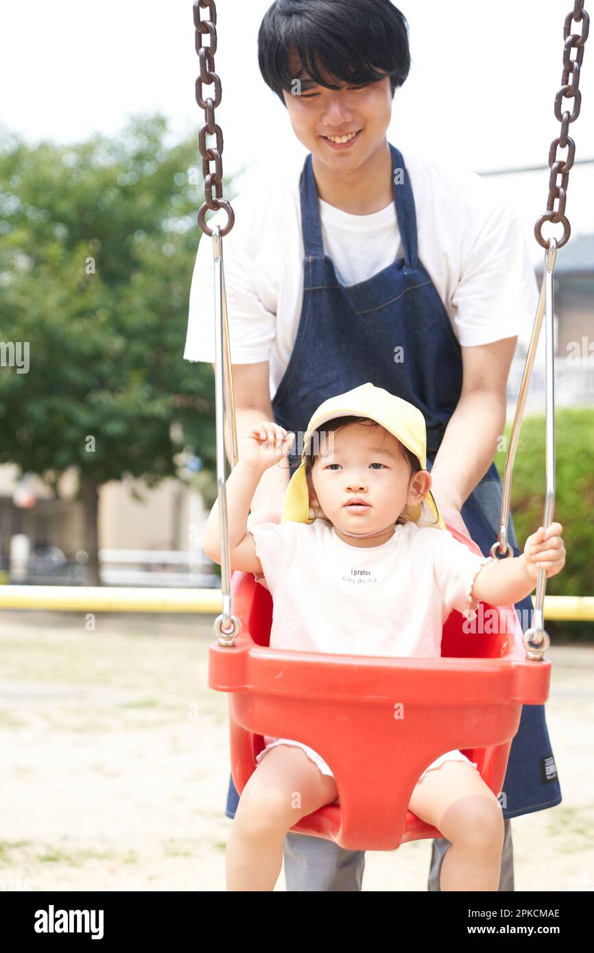 Male childcare worker with a child playing on a swing Stock Photo