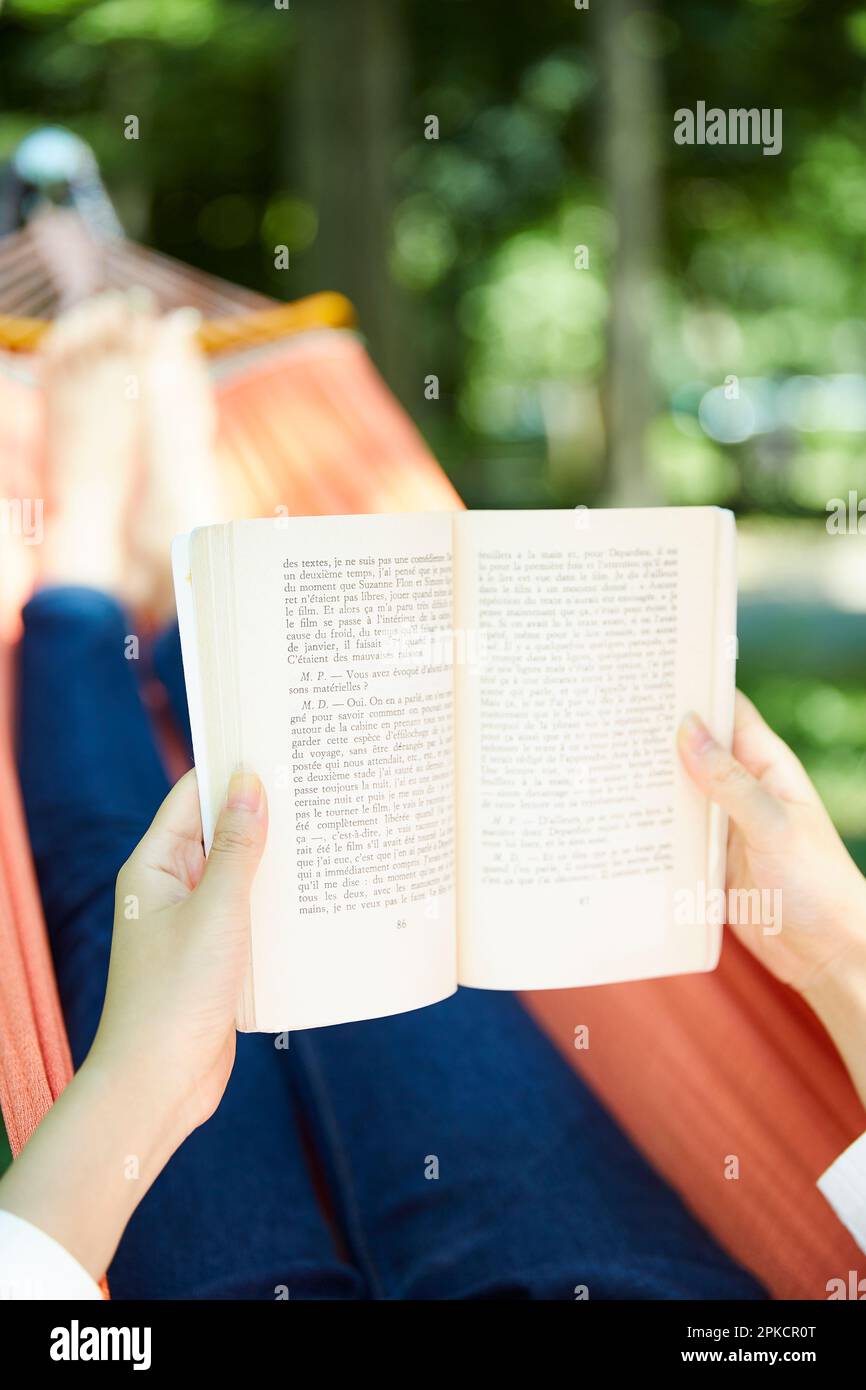 Hand of a woman reading a book lying in a hammock Stock Photo