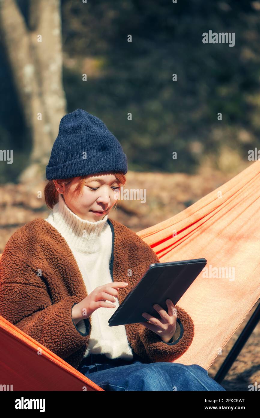 Woman operating a tablet device while sitting in a hammock Stock Photo