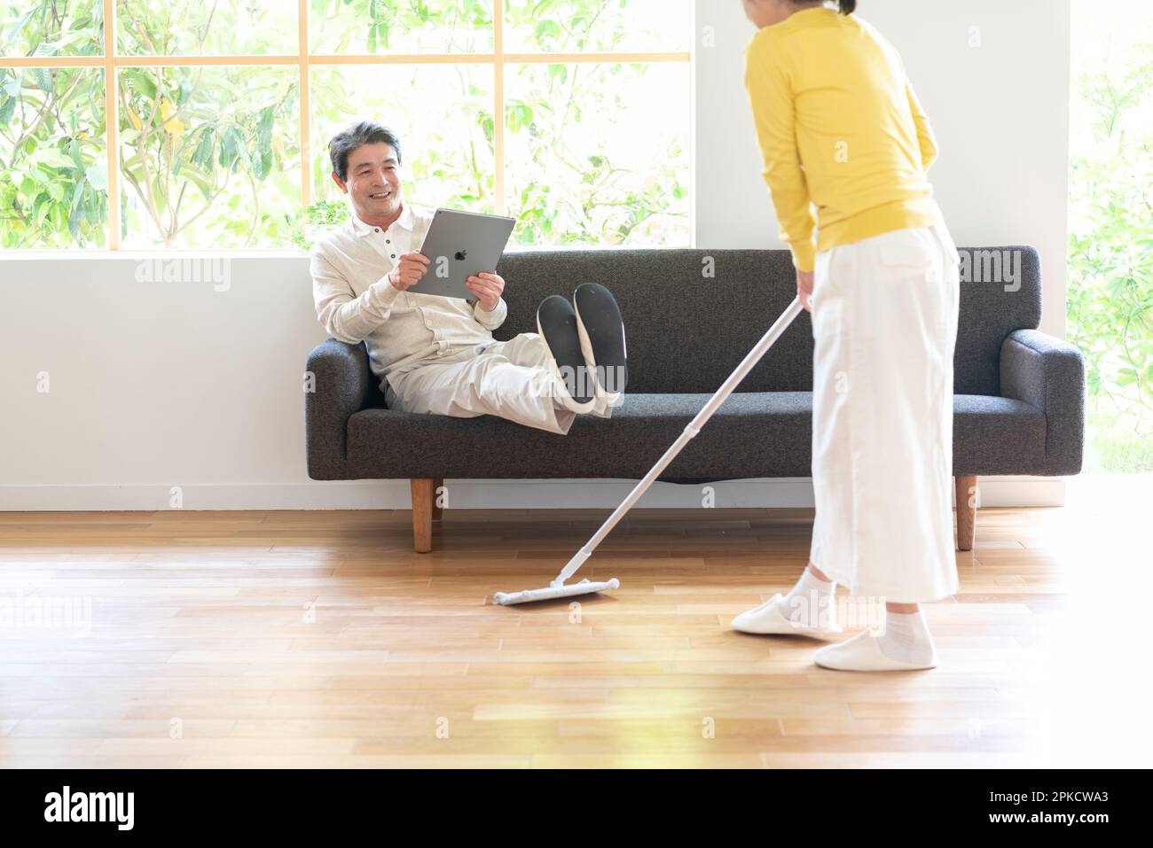 Middle-aged man watching PC on the sofa with a cleaning woman Stock ...