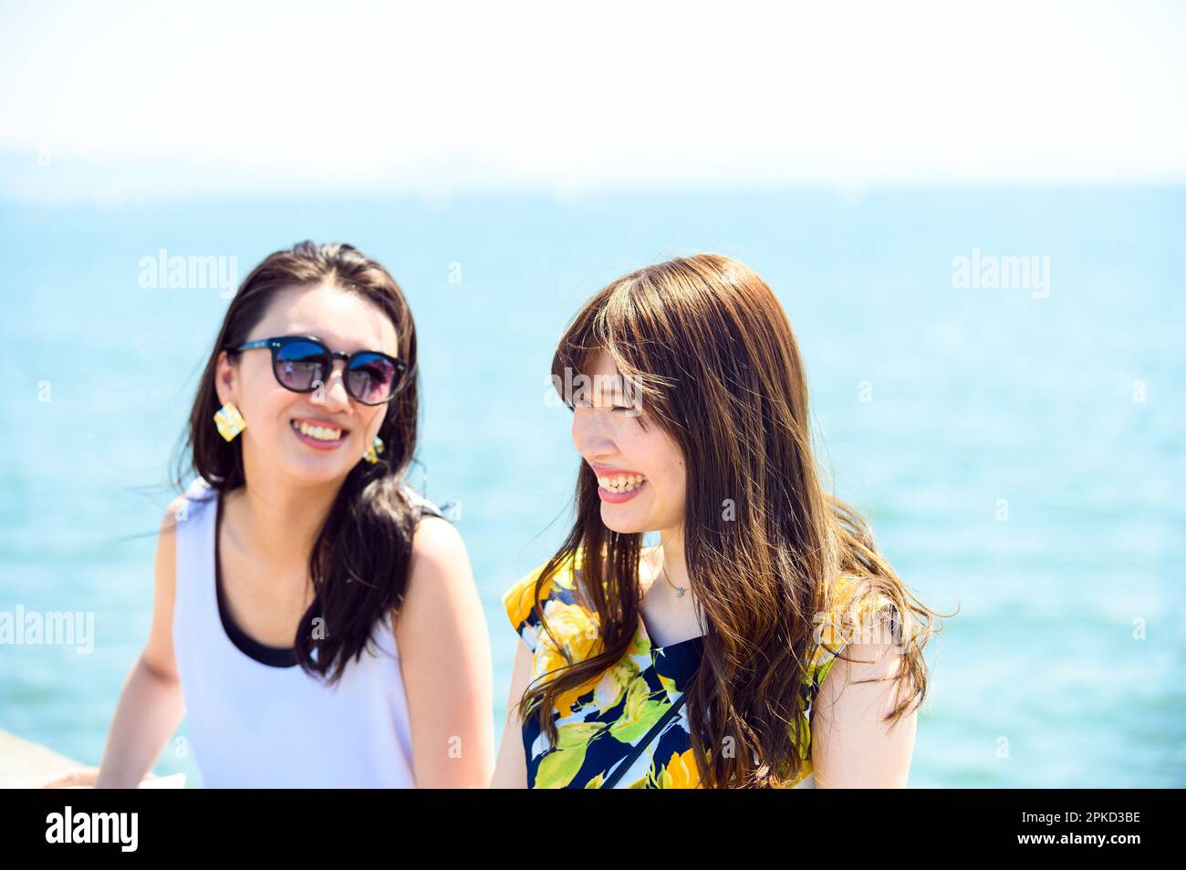 2 women traveling to a sea resort sitting on the harbor breakwater Stock Photo