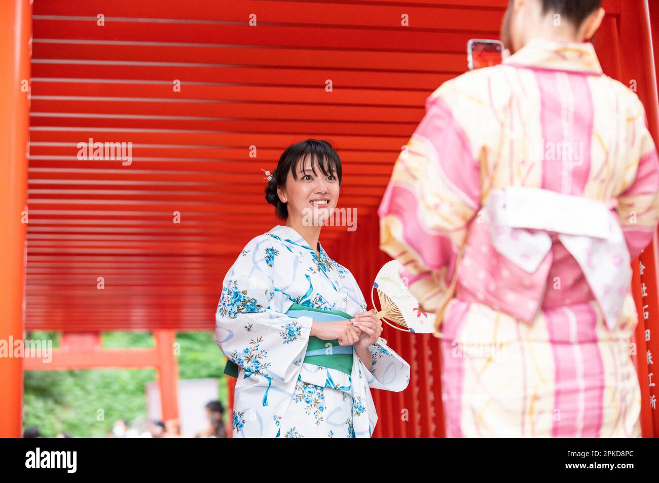 Two women in yukata taking a picture at the torii gate of a Shinto shrine Stock Photo