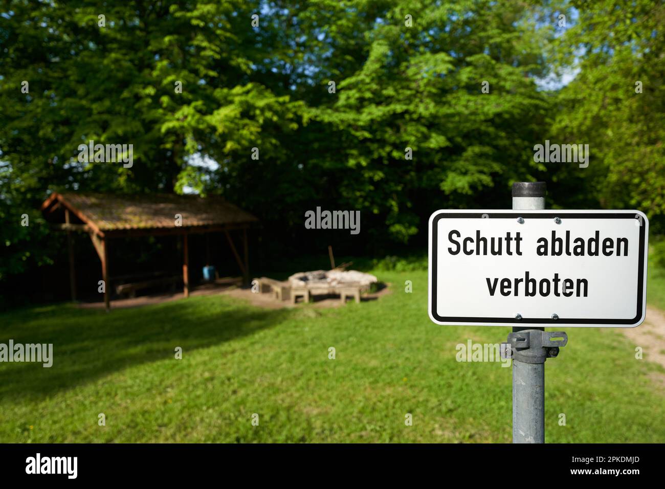 Rectangular sign in front of public barbecue saying: Dumping debris prohibited ( german: Schutt abladen verboten). Green meadow with fireplace and a w Stock Photo