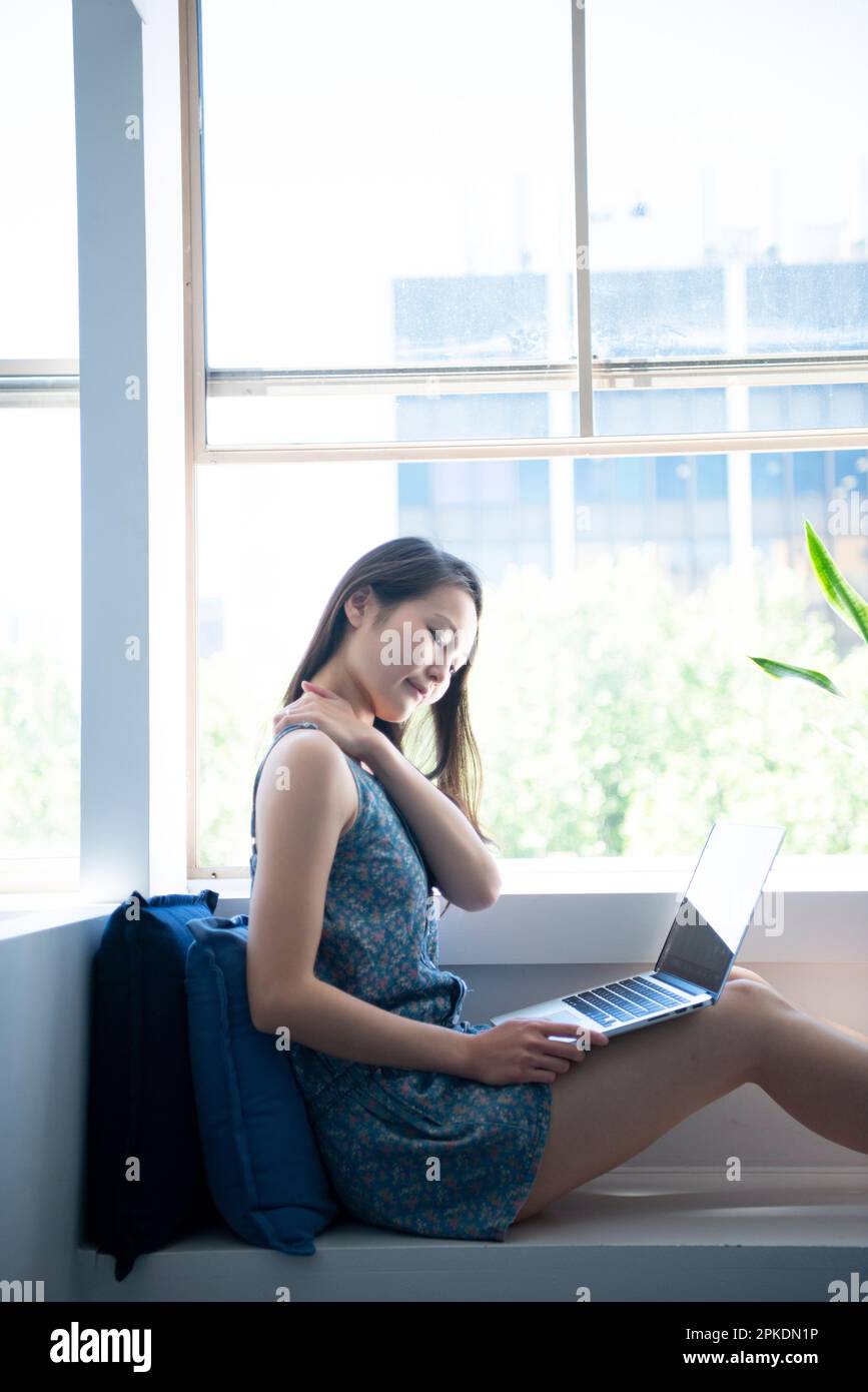 Woman touching her shoulder with computer on her leg Stock Photo - Alamy
