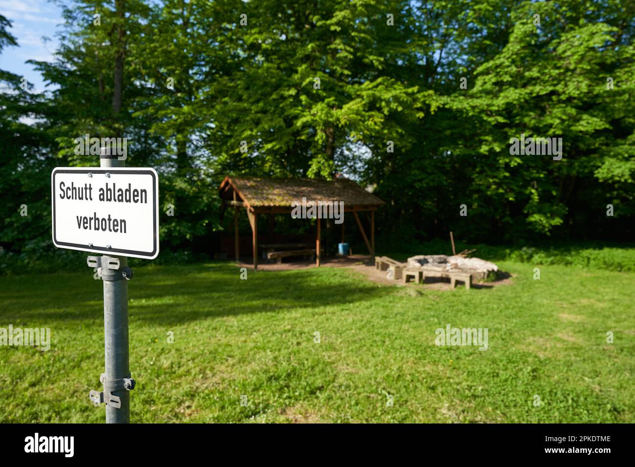 Rectangular sign in front of public barbecue saying: Dumping debris prohibited ( german: Schutt abladen verboten). Green meadow with fireplace and a w Stock Photo