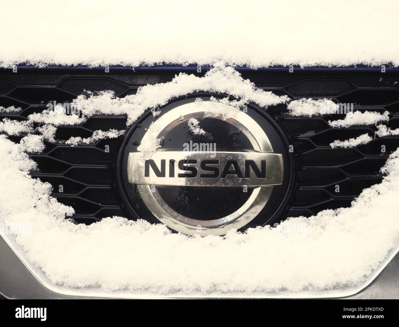 Front end of a Nissan car, covered in snow, showing the brand badge