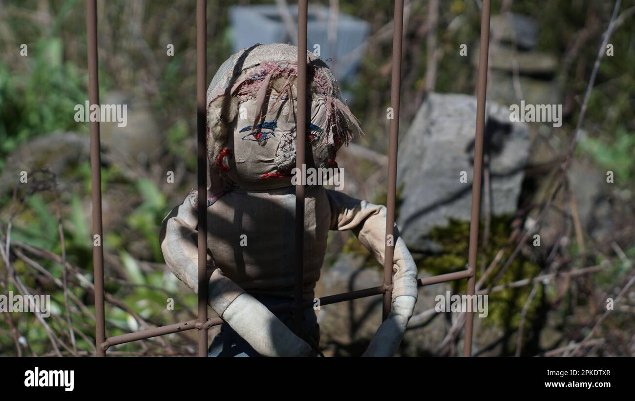 A worn ragdoll behind bars. With the shadow of a hand reaching for it. A sad and lost expression is on its face. Stock Photo