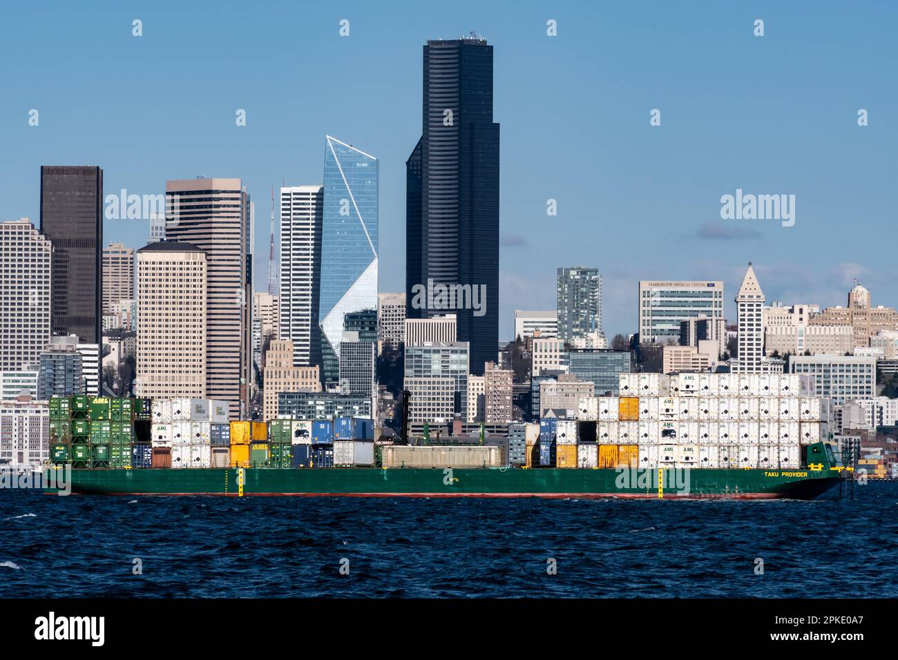 A container ship passes along the water in front of the Seattle downtown landscape on a clear sunny day Stock Photo