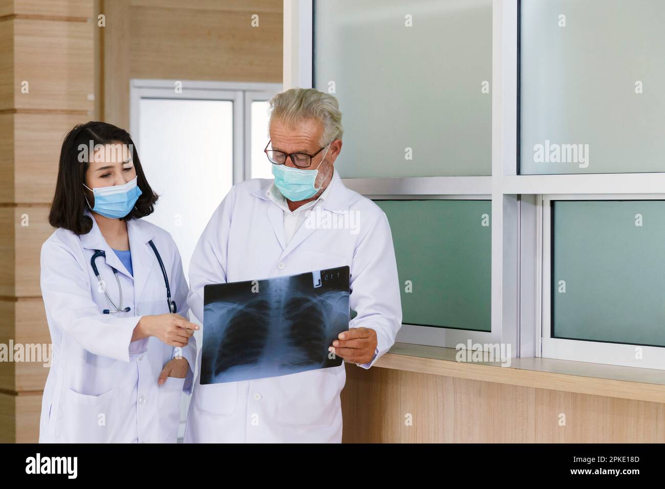 expertise senior surgical looking at x-ray film to give consult and discuss for surgery treatment the patient with young asian woman doctor in hospita Stock Photo