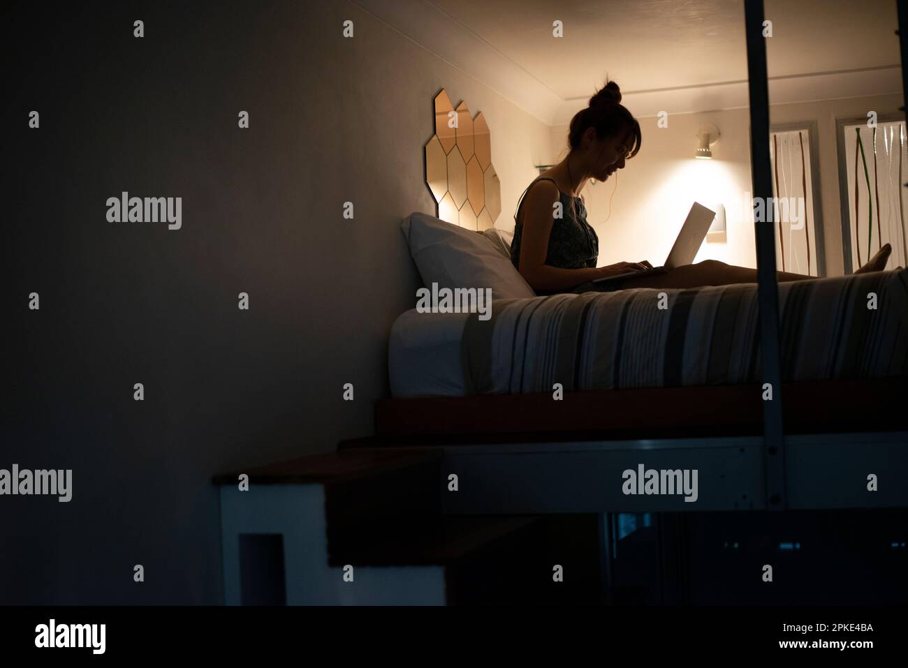 Woman using laptop on bed in loft Stock Photo