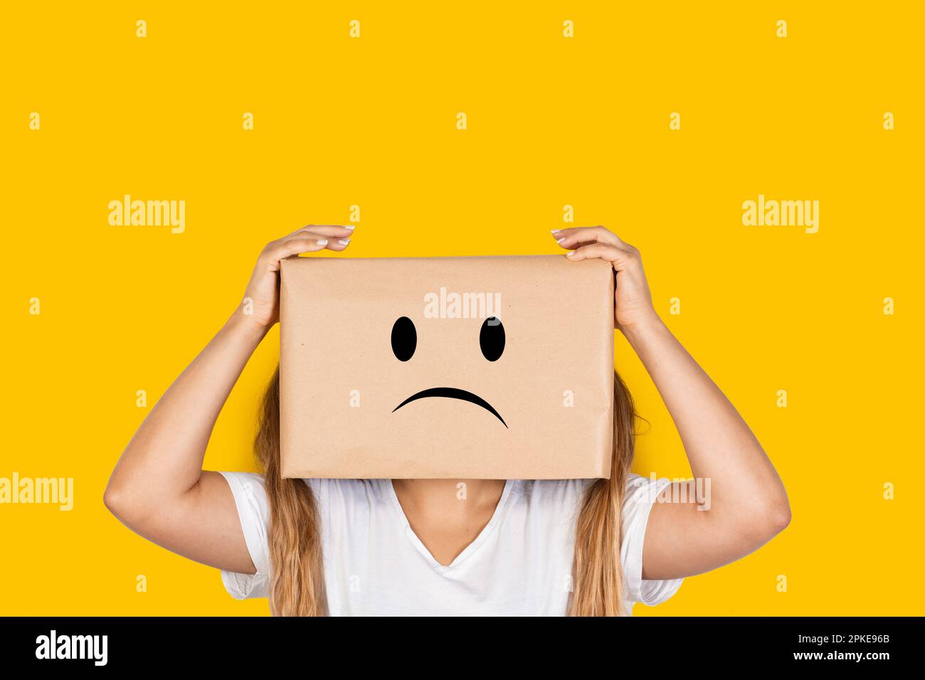 Woman with her head in a box, hands on it and sadness gesture on a yellow background with copy space Stock Photo