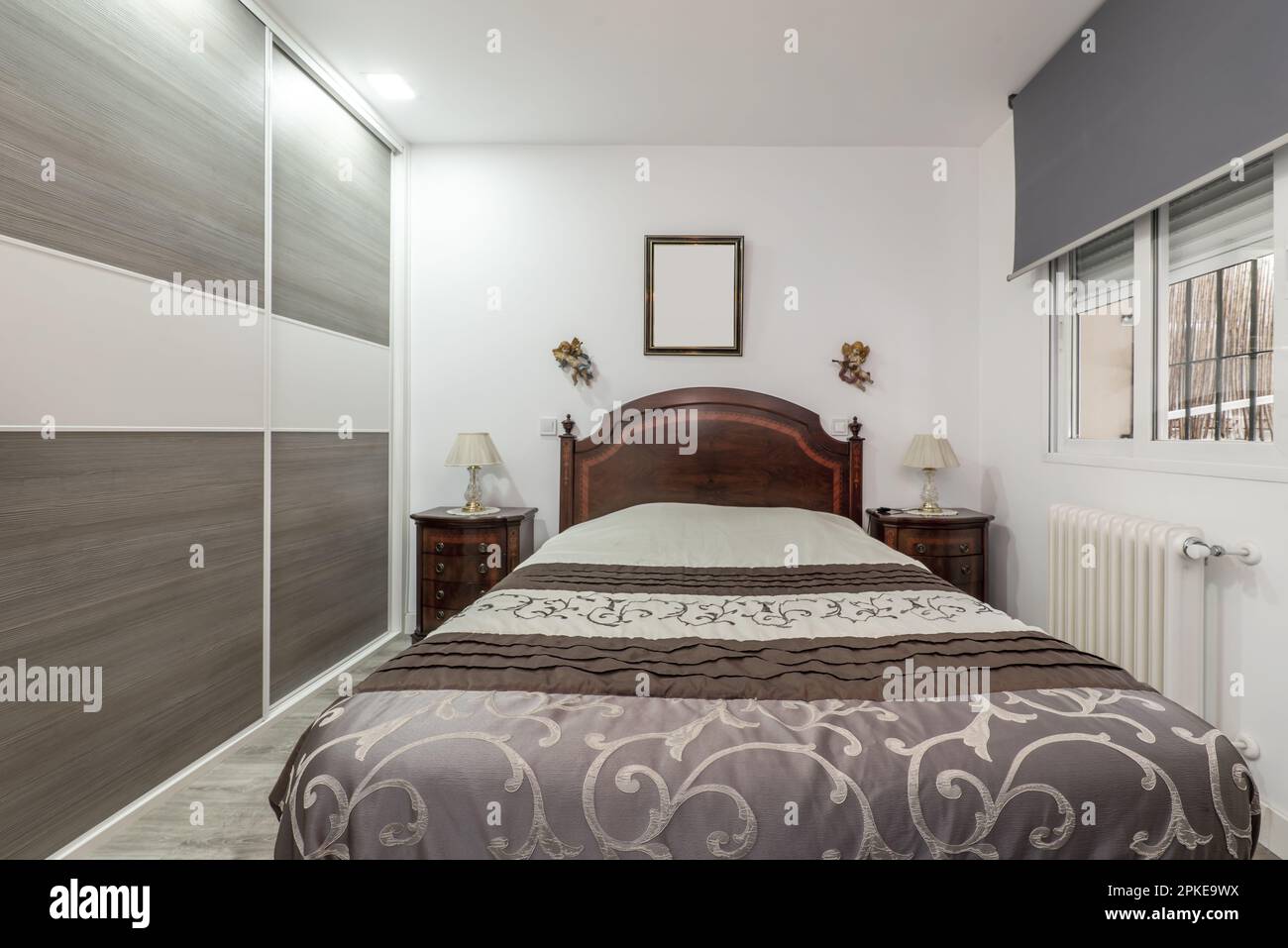Double bedroom with conventional classic decoration, built-in gray wardrobe with sliding doors and bedside tables made of varnished root wood Stock Photo