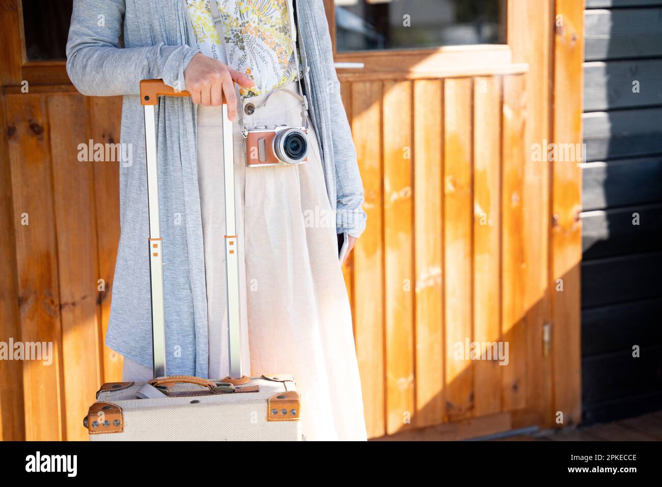 Woman in front of door with suitcase and camera Stock Photo