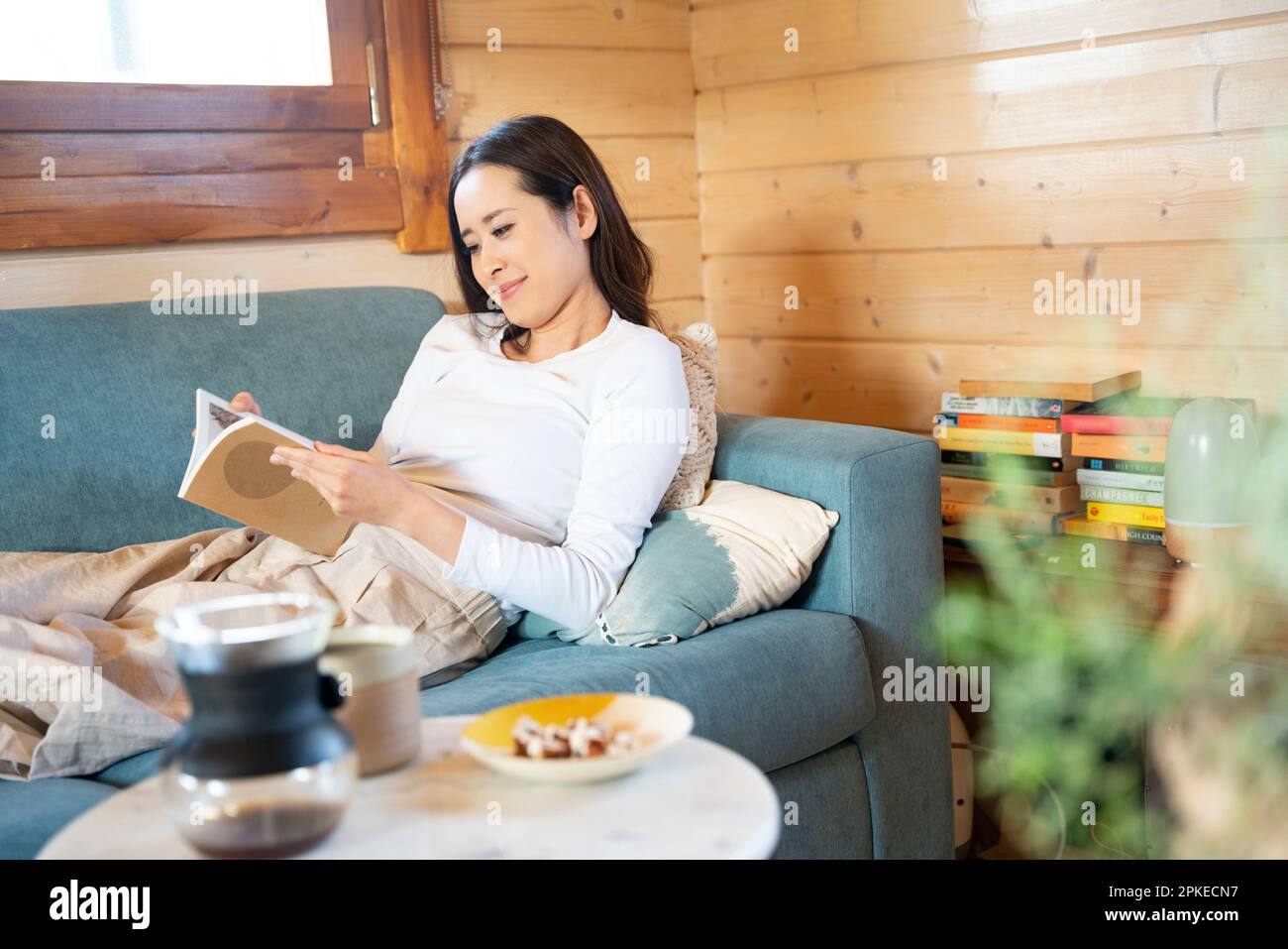 Woman sitting on the sofa reading a book Stock Photo Alamy