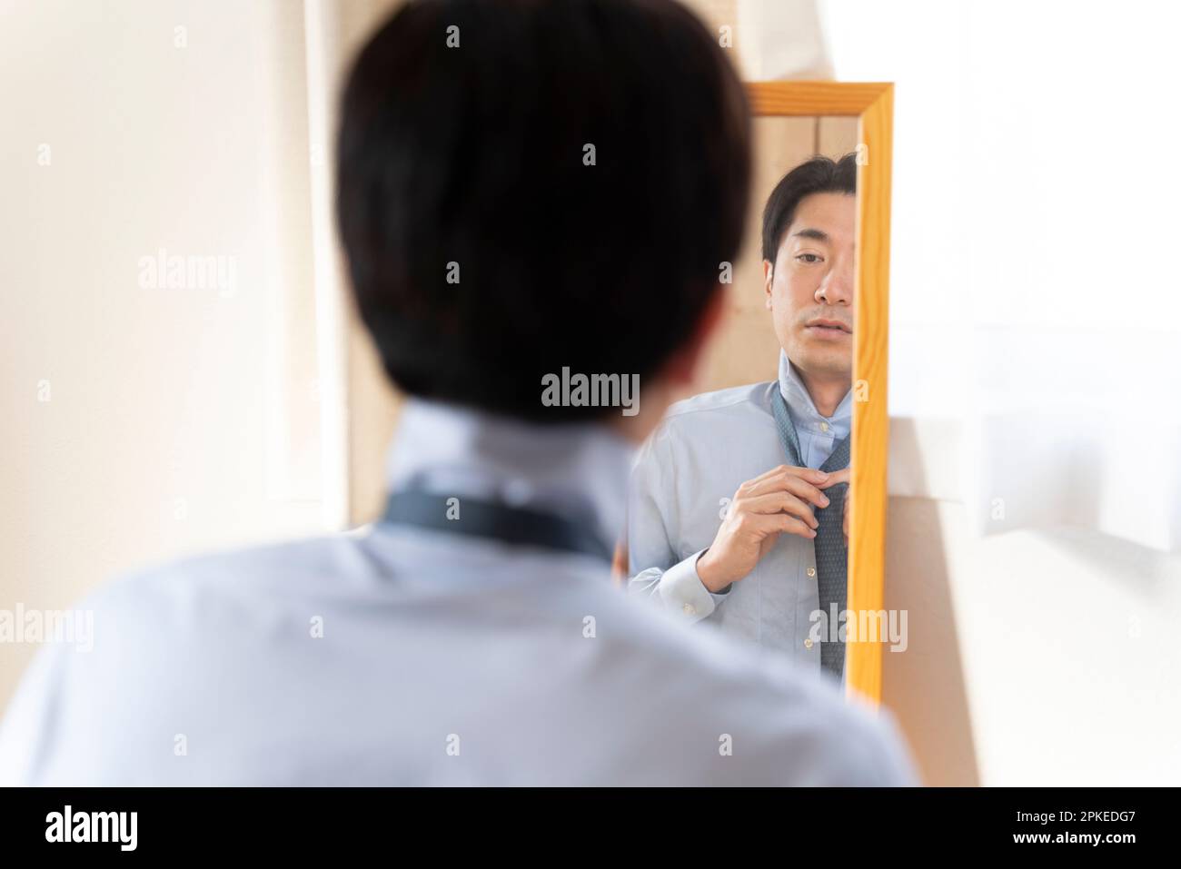 Man putting on tie while looking in mirror Stock Photo