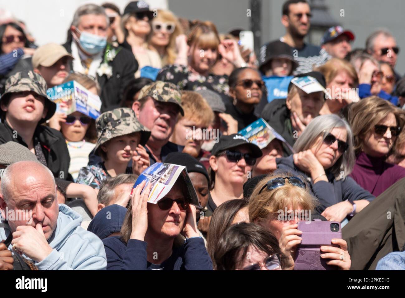 Trafalgar Square, Westminster, London, UK. 7th Apr, 2023. The day has begun warm and sunny, with people using event programmes for shade during the performance of The Passion of Jesus in Trafalgar Square. Free public event. Stock Photo