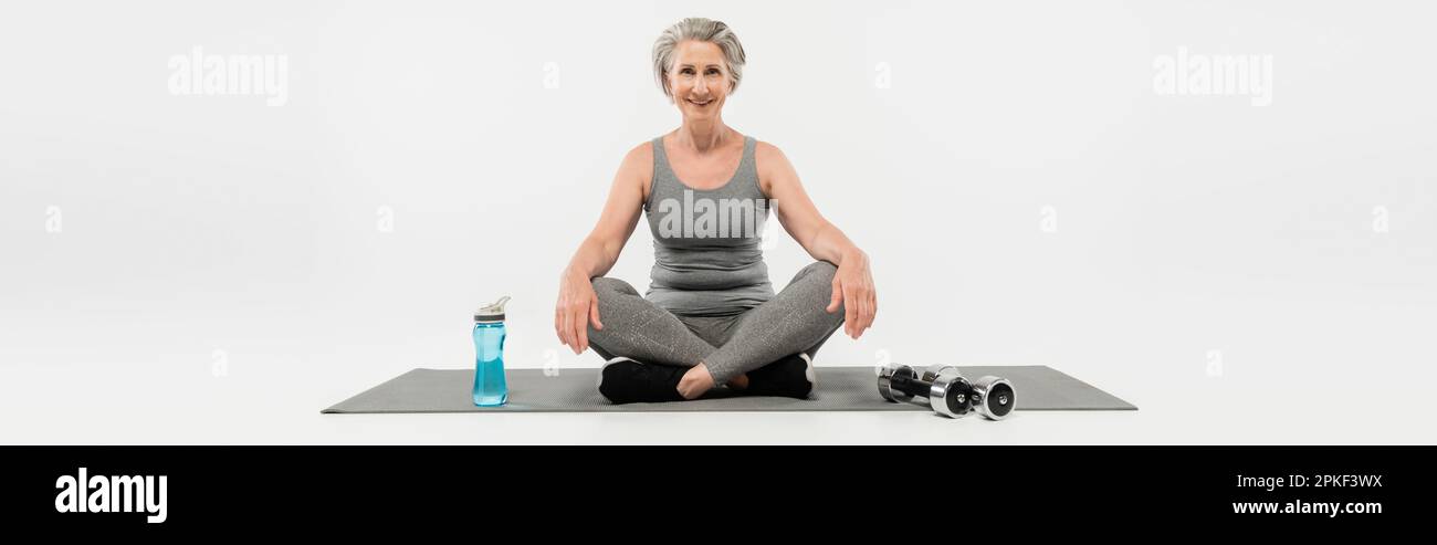 senior woman with wireless earphones sitting in yoga pose on mat
