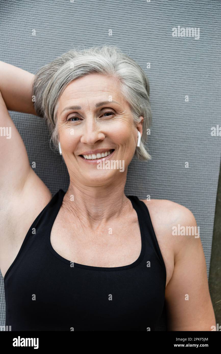 top view of happy senior woman in wireless earphones lying on fitness mat,stock image Stock Photo