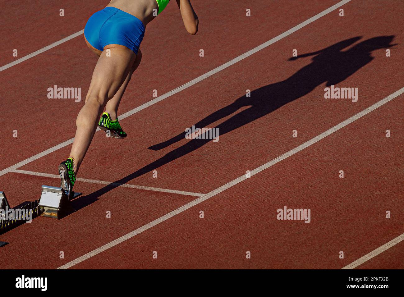 start female athlete from starting blocks running sprint distance, shadow woman runner on stadium track Stock Photo