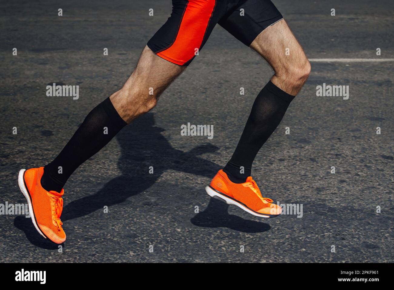 legs male runner in black compression socks and bright running shoes, shadow man jogger in dark asphalt Stock Photo