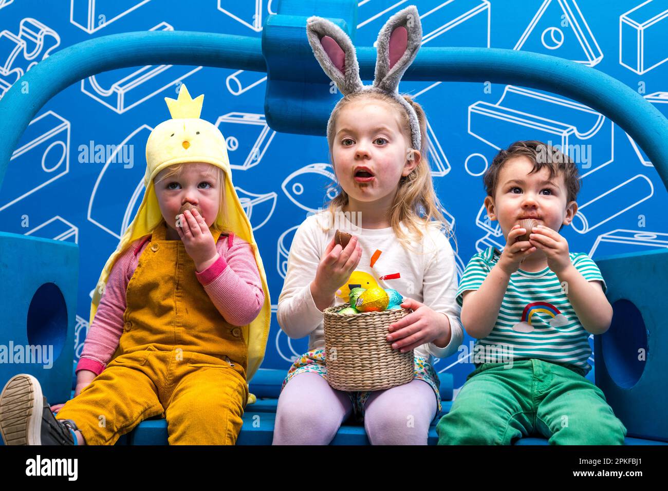 Three happy young children eating chocolate Easter eggs at Edinburgh Science Festival, Scotland, UK Stock Photo