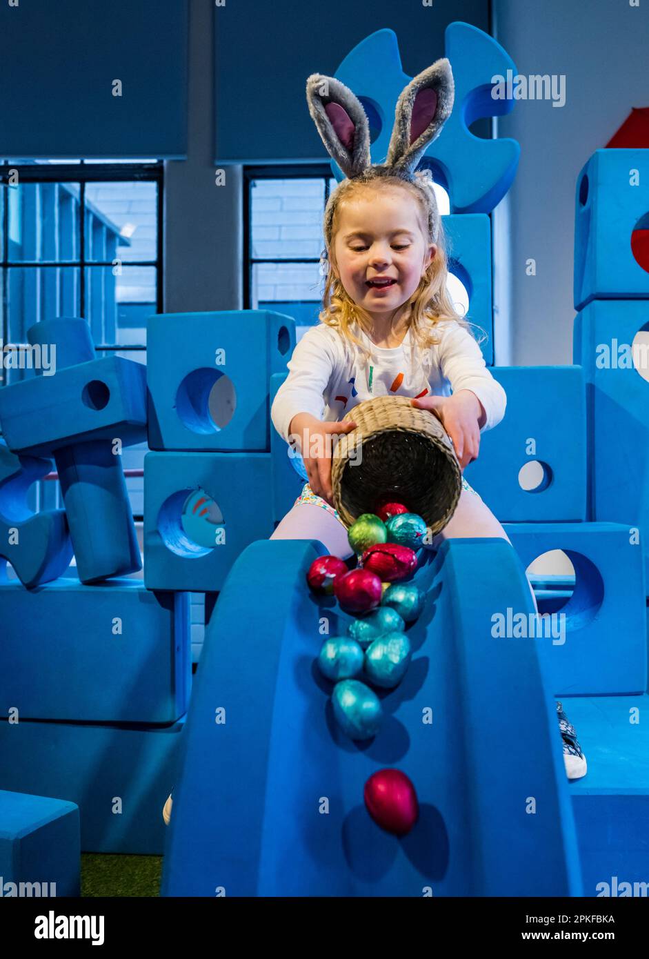 Young girl having fun rolling chocolate Easter eggs down slide, Edinburgh Science Festival, Scotland, UK Stock Photo