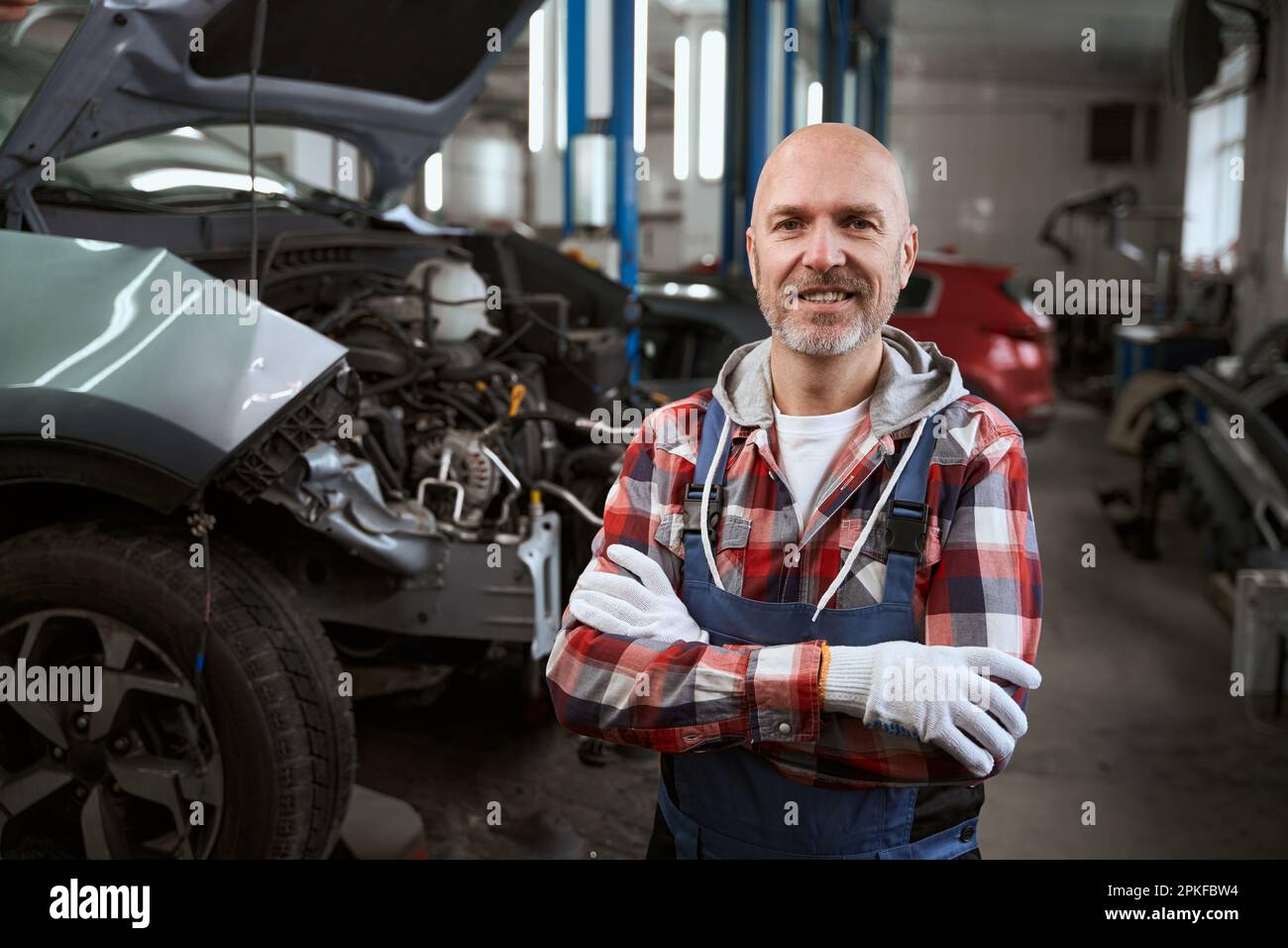 Smiling auto repairman stands at his workplace against background of cars Stock Photo