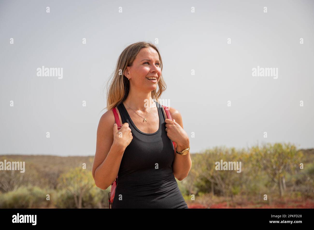 A smiling female hiker looks around on a hike during a hot summer day. Stock Photo