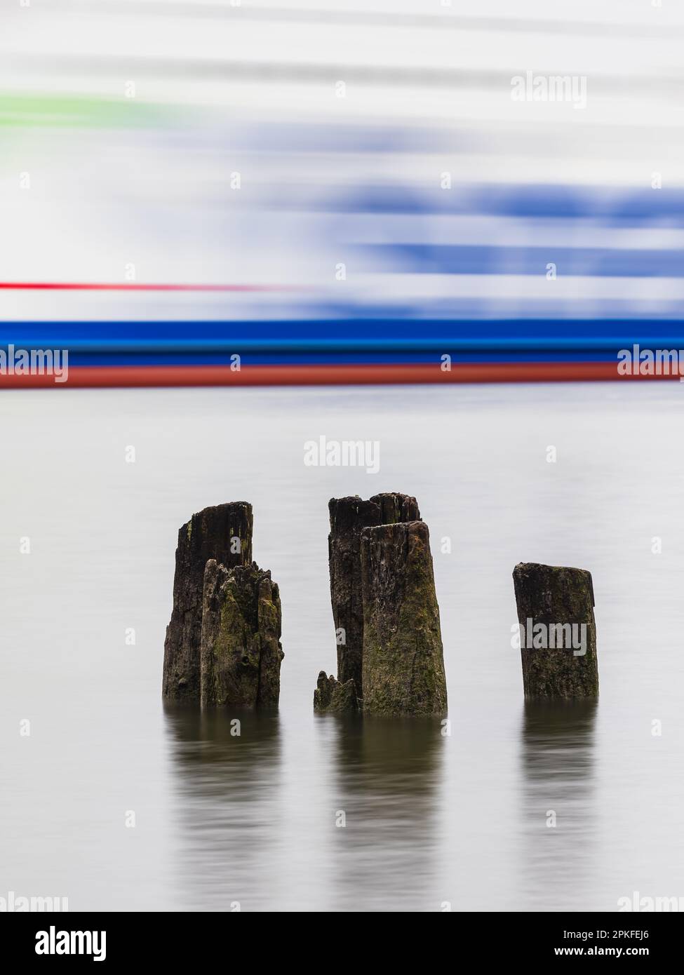 A long exposure photo of a ferry drifting behind wooden poles in the peaceful Göta River in Gothenburg, Sweden. Stock Photo