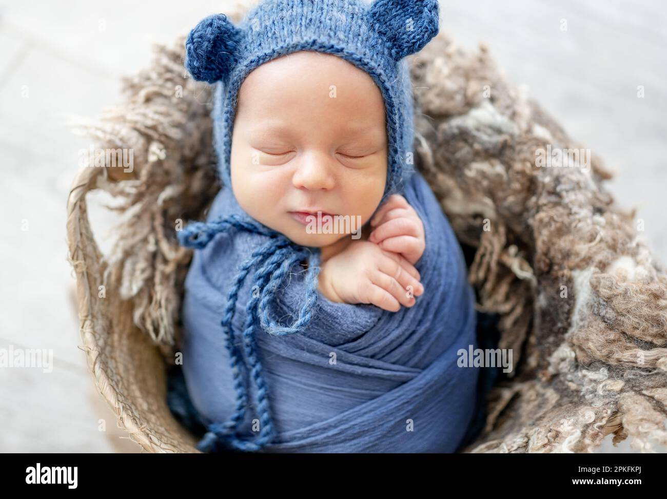 Newborn baby boy sleeping swaddled in blue fabric and wearing hat in